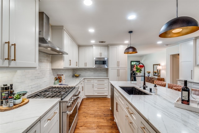 kitchen with tasteful backsplash, light wood-type flooring, wall chimney range hood, stainless steel appliances, and pendant lighting