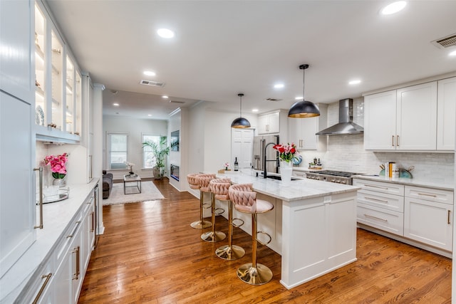 kitchen featuring white cabinetry, wall chimney exhaust hood, a center island with sink, light hardwood / wood-style flooring, and backsplash