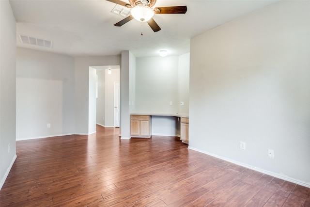 empty room featuring dark wood-type flooring, built in desk, and ceiling fan