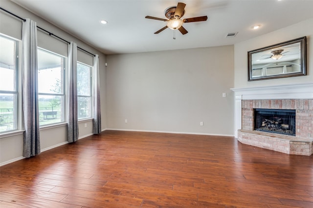 unfurnished living room featuring ceiling fan, a brick fireplace, and dark hardwood / wood-style flooring