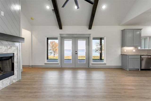 unfurnished living room with french doors, vaulted ceiling with beams, ceiling fan, a fireplace, and light hardwood / wood-style floors