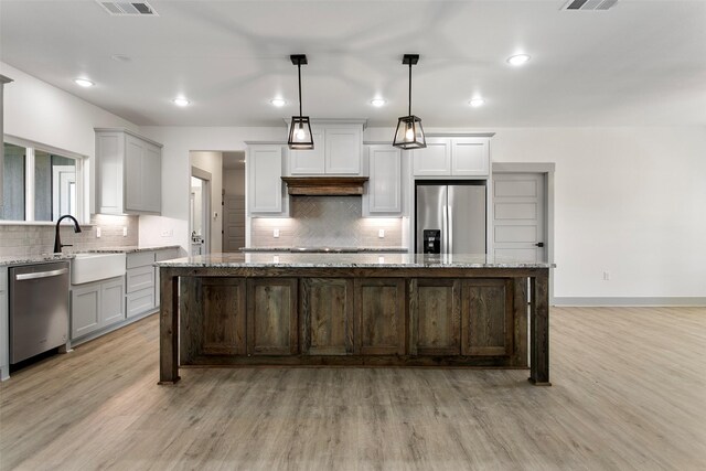 kitchen with pendant lighting, light wood-type flooring, stainless steel appliances, and a kitchen island