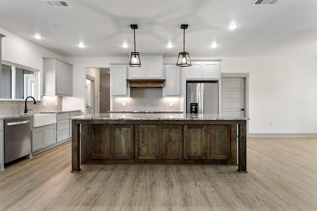 kitchen with light stone counters, appliances with stainless steel finishes, hanging light fixtures, and a kitchen island