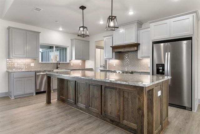 kitchen featuring pendant lighting, stainless steel appliances, a center island, and light stone countertops