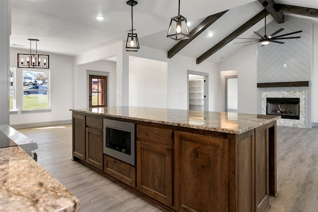 kitchen featuring built in microwave, vaulted ceiling with beams, hanging light fixtures, a kitchen island, and light stone countertops