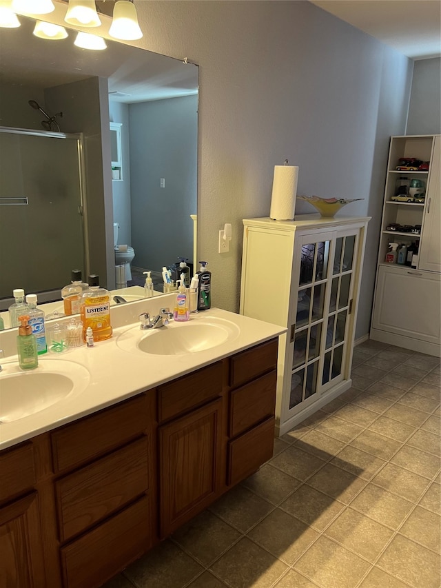 bathroom featuring a shower with shower door, double vanity, toilet, and tile patterned floors