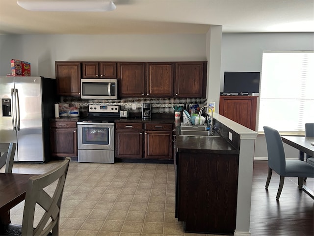 kitchen featuring tasteful backsplash, kitchen peninsula, stainless steel appliances, light hardwood / wood-style floors, and sink