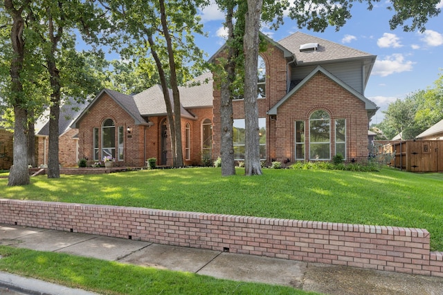 view of front of home featuring a shingled roof, a front yard, and brick siding