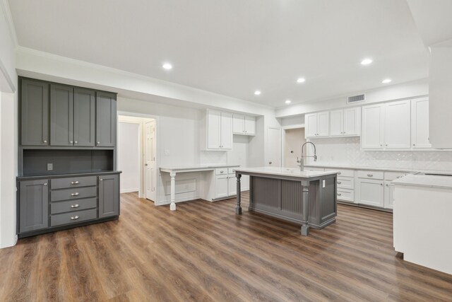 kitchen with decorative backsplash, gray cabinetry, a kitchen island with sink, a kitchen breakfast bar, and dark wood-type flooring