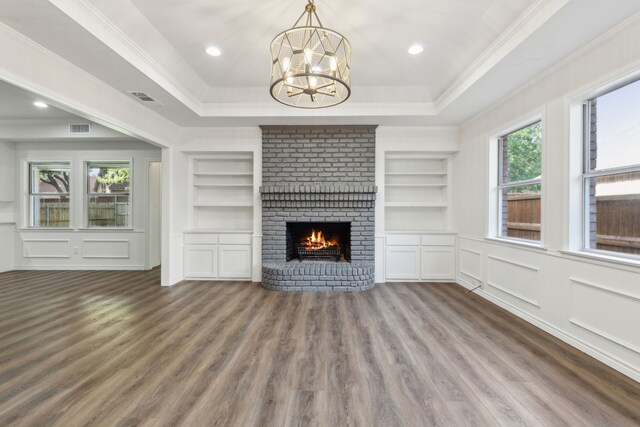 unfurnished living room featuring a notable chandelier, a tray ceiling, crown molding, hardwood / wood-style floors, and a brick fireplace