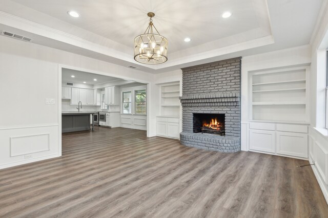 unfurnished living room with a fireplace, hardwood / wood-style floors, ornamental molding, sink, and a raised ceiling