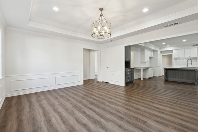 unfurnished living room featuring sink, a chandelier, a tray ceiling, and hardwood / wood-style floors