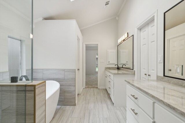 bathroom with tile walls, a washtub, crown molding, lofted ceiling, and vanity