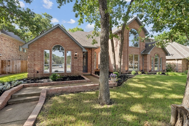 view of front of house with brick siding, a front yard, fence, and a shingled roof