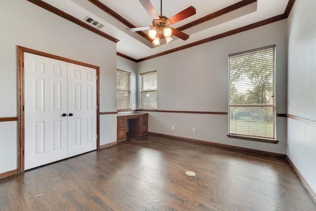 unfurnished bedroom featuring dark hardwood / wood-style floors, built in desk, ornamental molding, a tray ceiling, and a closet