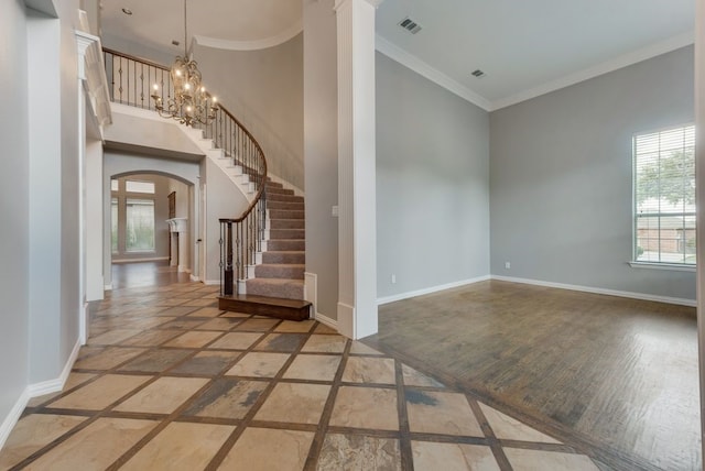 entryway with crown molding, wood-type flooring, a wealth of natural light, and a notable chandelier