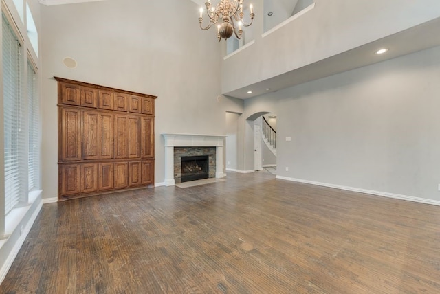 unfurnished living room featuring dark wood-type flooring, a notable chandelier, a fireplace, and a towering ceiling