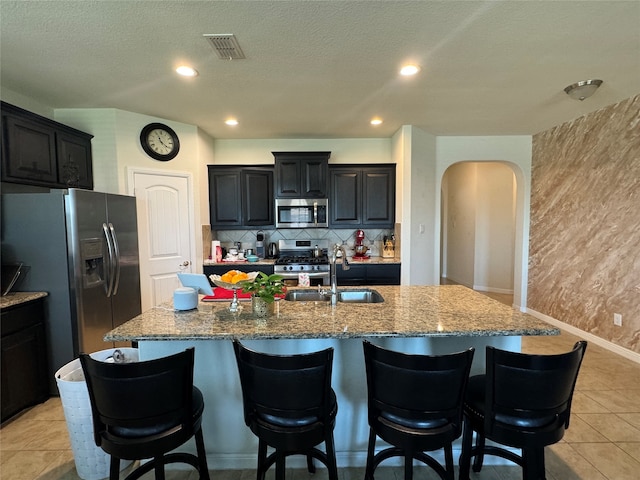 kitchen with sink, a kitchen island with sink, a breakfast bar, light tile patterned flooring, and appliances with stainless steel finishes