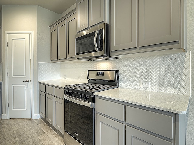 kitchen featuring decorative backsplash, appliances with stainless steel finishes, light stone counters, and gray cabinetry