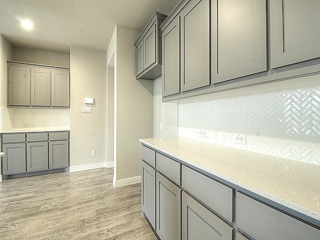 kitchen with decorative backsplash, light stone countertops, light hardwood / wood-style flooring, and gray cabinetry