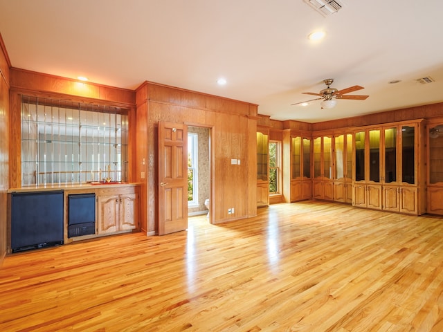 unfurnished living room with light hardwood / wood-style floors, ceiling fan, and wooden walls