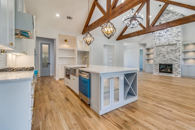 kitchen featuring dishwasher, built in features, decorative light fixtures, a fireplace, and a center island with sink