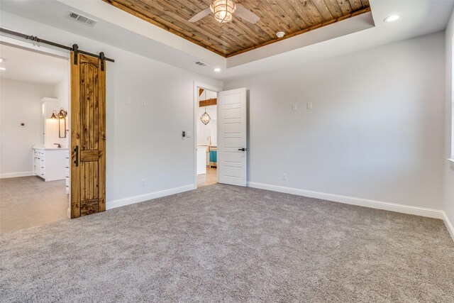 empty room featuring ceiling fan, a raised ceiling, a barn door, light colored carpet, and wood ceiling