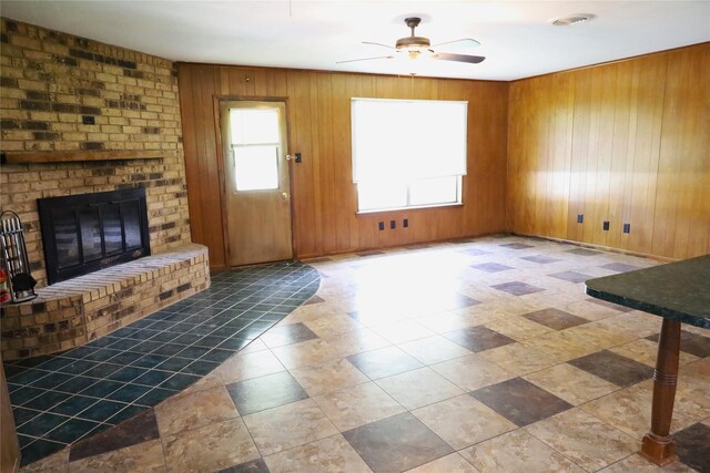 unfurnished living room featuring tile patterned flooring, wood walls, ceiling fan, brick wall, and a fireplace