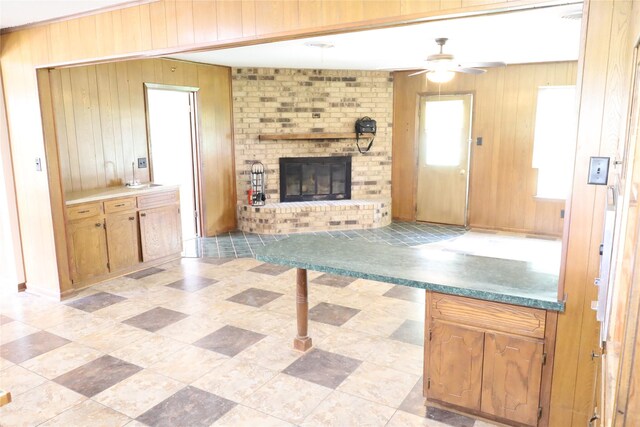 unfurnished living room featuring light tile patterned floors, wood walls, ceiling fan, a brick fireplace, and brick wall