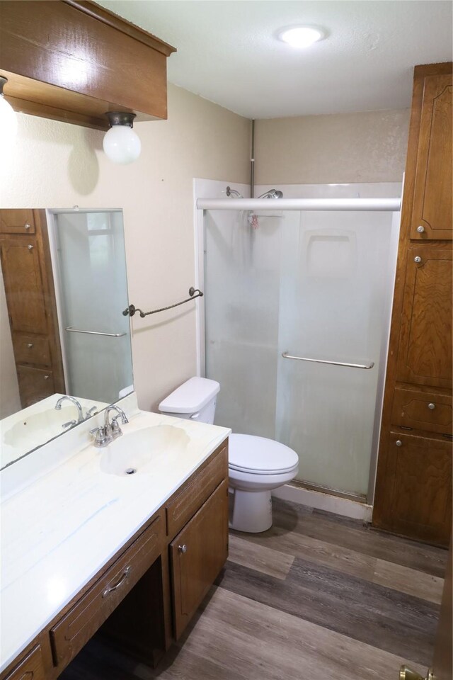 bathroom featuring a shower with shower door, vanity, wood-type flooring, and toilet