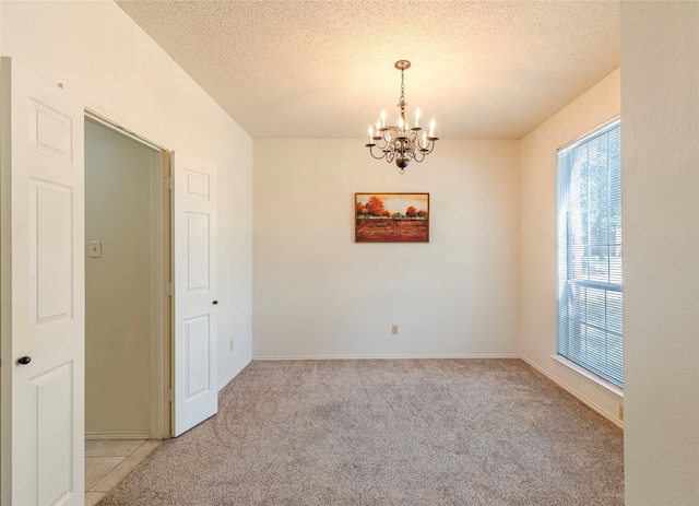 unfurnished room with a textured ceiling, light colored carpet, and a notable chandelier