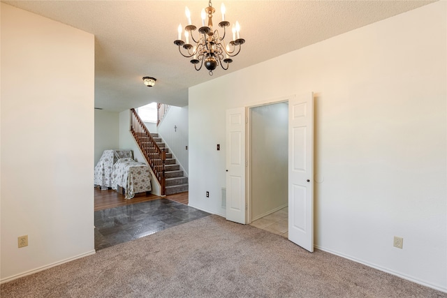 carpeted empty room featuring a textured ceiling and an inviting chandelier