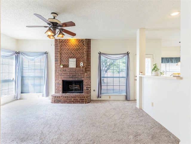 unfurnished living room with ceiling fan, carpet floors, a textured ceiling, and a brick fireplace