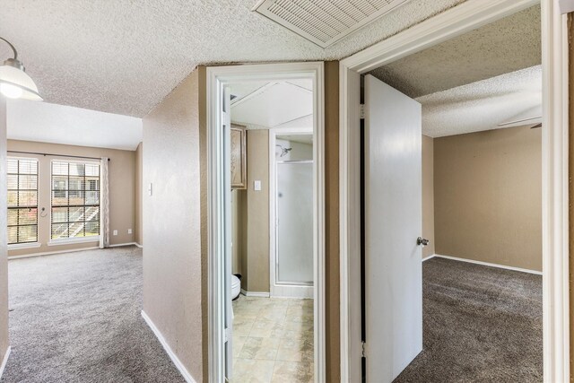 hall with vaulted ceiling, light colored carpet, and a textured ceiling