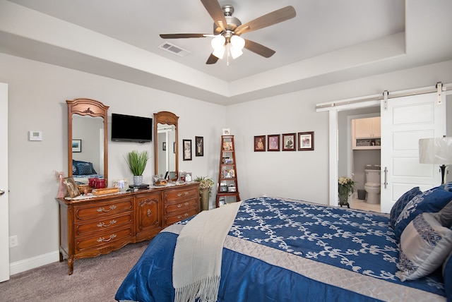 bedroom featuring connected bathroom, ceiling fan, a tray ceiling, a barn door, and carpet