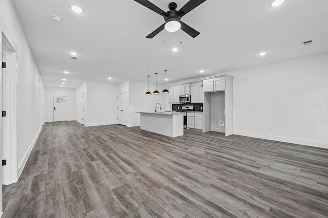 interior space with hanging light fixtures, hardwood / wood-style flooring, stainless steel appliances, an island with sink, and ceiling fan