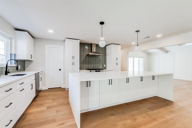 kitchen with sink, light wood-type flooring, wall chimney range hood, and backsplash