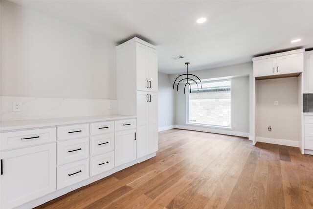 kitchen featuring white cabinets, hanging light fixtures, and light hardwood / wood-style flooring