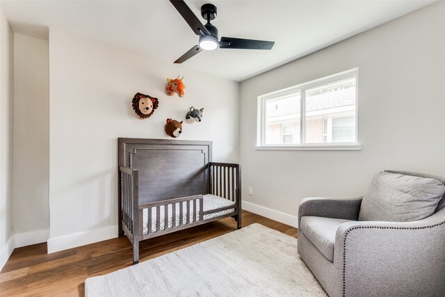 bedroom with ceiling fan, a nursery area, and wood-type flooring