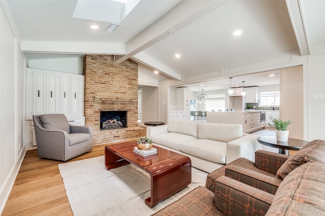 living room featuring sink, a brick fireplace, a notable chandelier, vaulted ceiling with skylight, and light wood-type flooring