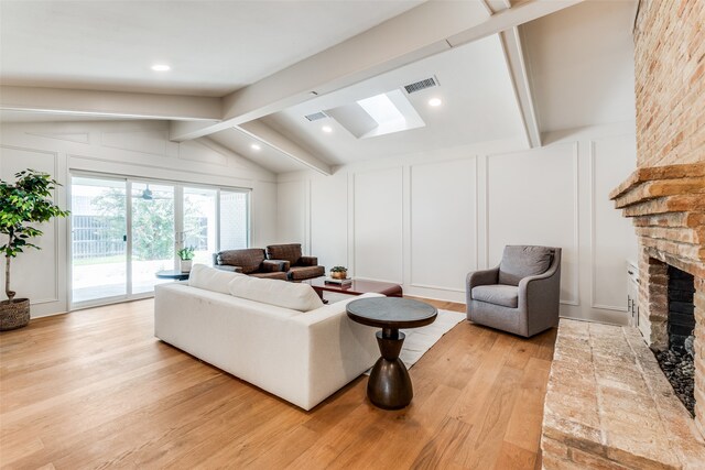 living room with lofted ceiling with beams, light hardwood / wood-style floors, and a brick fireplace