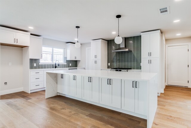 kitchen featuring decorative light fixtures, a kitchen island, white cabinetry, and light hardwood / wood-style flooring