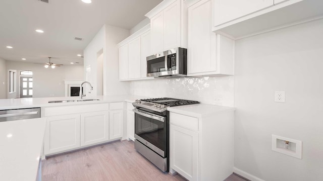 kitchen with ceiling fan, sink, stainless steel appliances, kitchen peninsula, and white cabinets