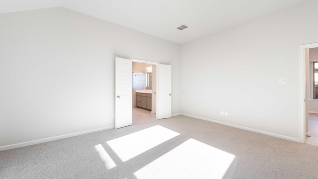 unfurnished bedroom featuring ensuite bathroom, light colored carpet, and vaulted ceiling