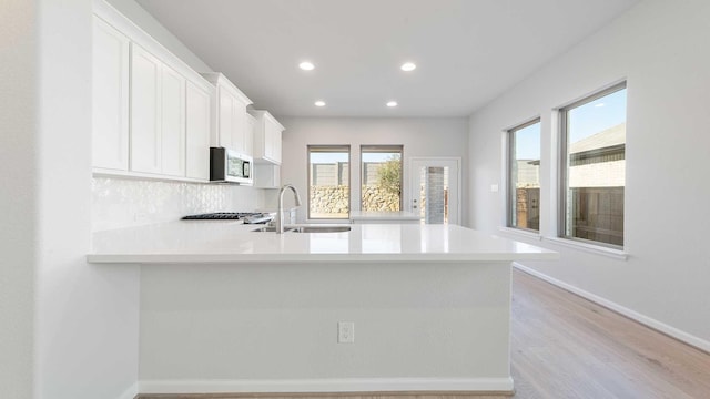 kitchen featuring kitchen peninsula, white cabinetry, sink, and light hardwood / wood-style flooring