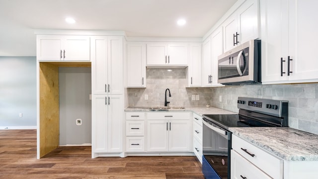 kitchen with tasteful backsplash, white cabinets, light stone counters, hardwood / wood-style floors, and appliances with stainless steel finishes