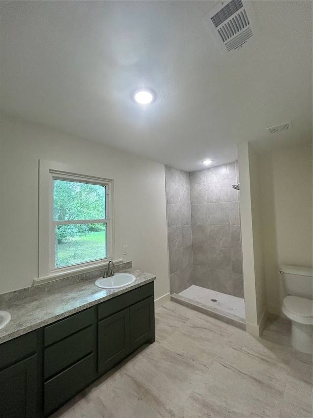 bathroom featuring vanity, toilet, a tile shower, and tile patterned flooring