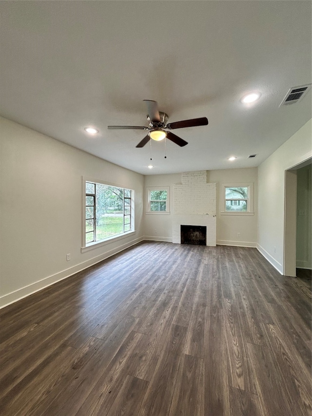 unfurnished living room with a fireplace, dark wood-type flooring, ceiling fan, and brick wall