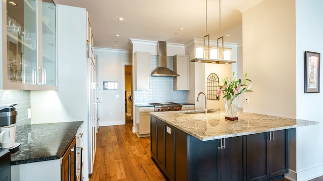 kitchen with sink, decorative light fixtures, decorative backsplash, light wood-type flooring, and wall chimney exhaust hood