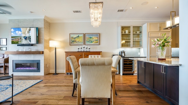 dining room with an inviting chandelier, a fireplace, wine cooler, and light hardwood / wood-style floors